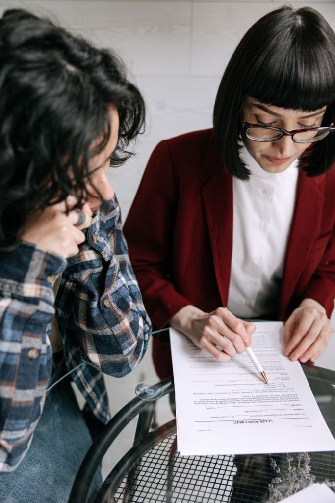 Two women consulting over legal papers indoors, discussing financial decisions.